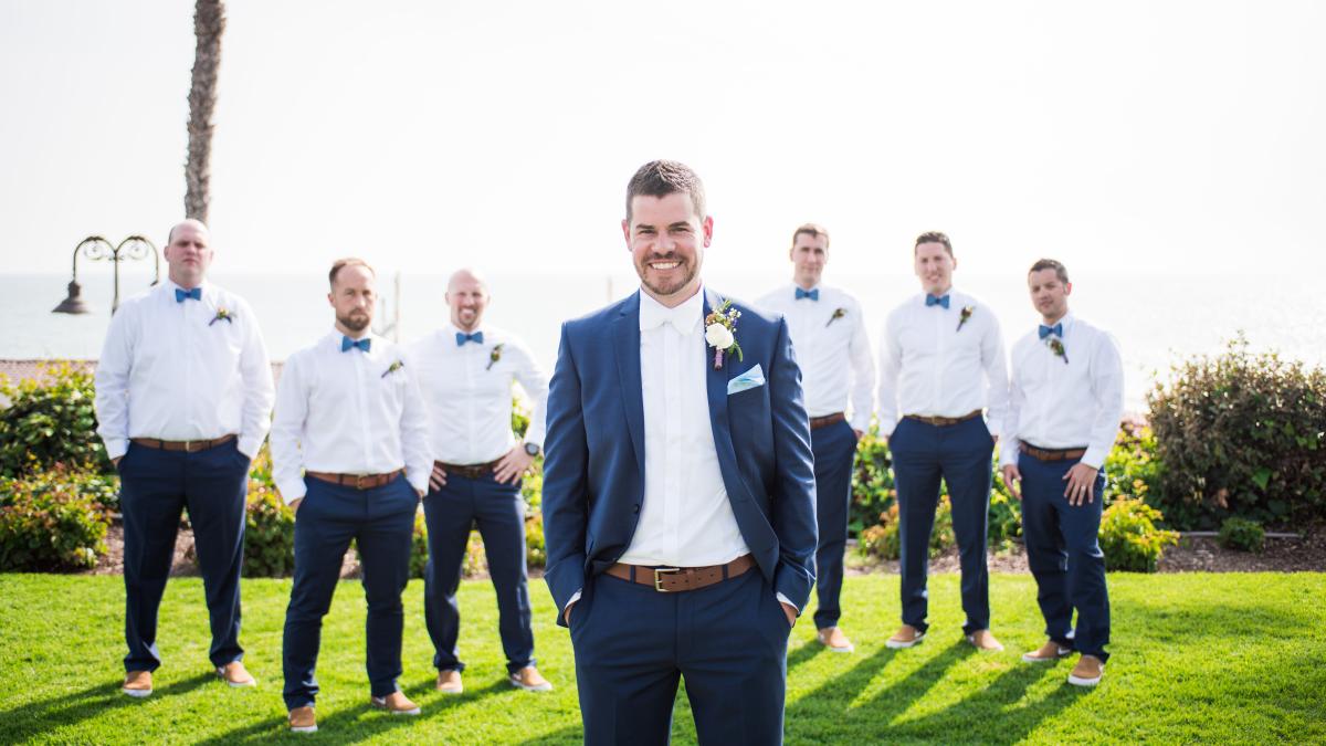 A groom and groomsmen stand next to each and other and pose in the Ole Hanson Beach Club Grand Lawn
