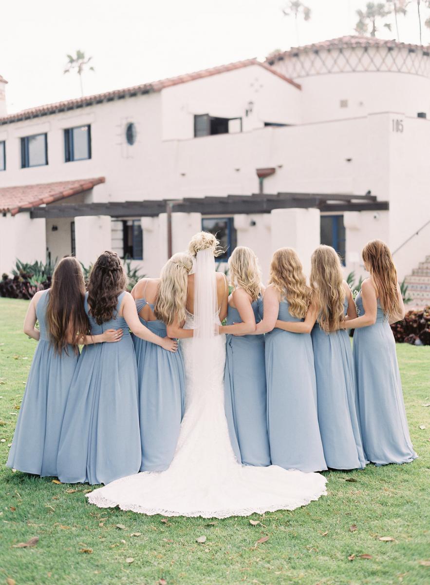 A bride and bridesmaids link arms and stand together facing the Ole Hanson Beach Club building