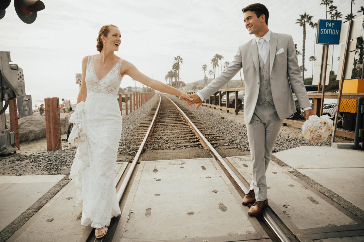 A cheerful couple walks and holds hands along the train tracks